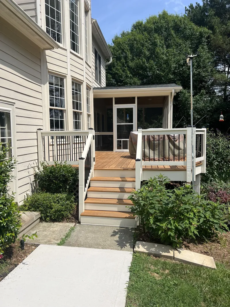 Wood steps and a railed deck leading up to a screened porch beside the house