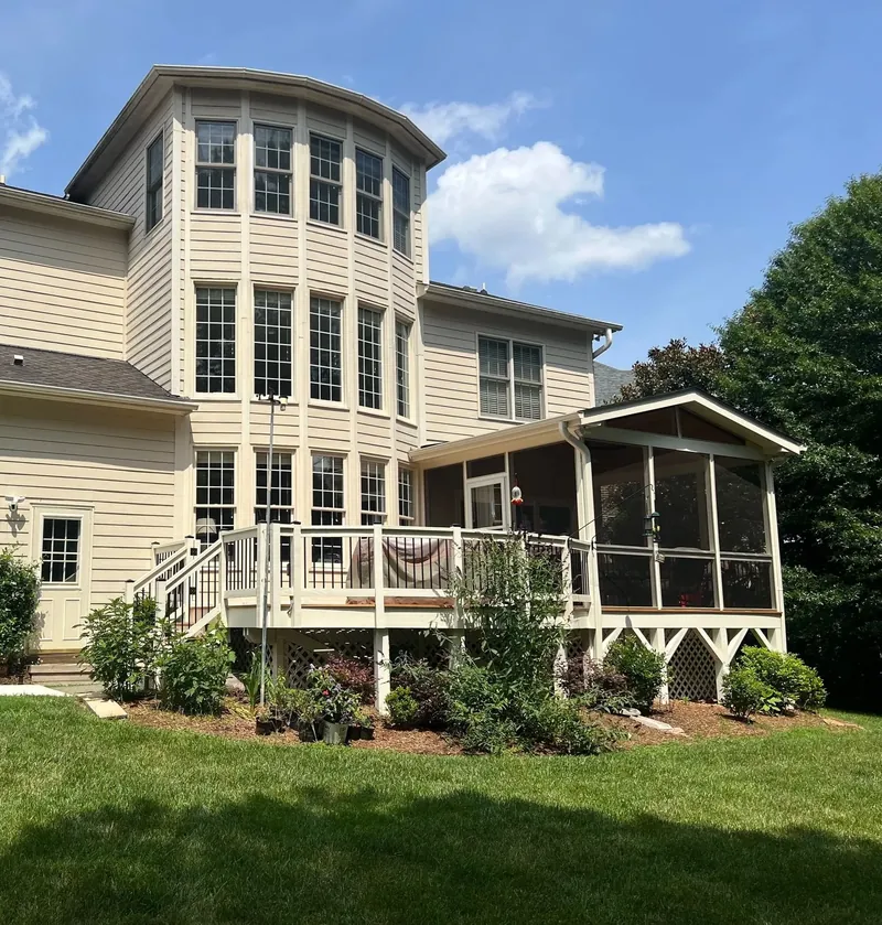 Backyard deck with white railings joined to a gable roof screened porch on a two story home